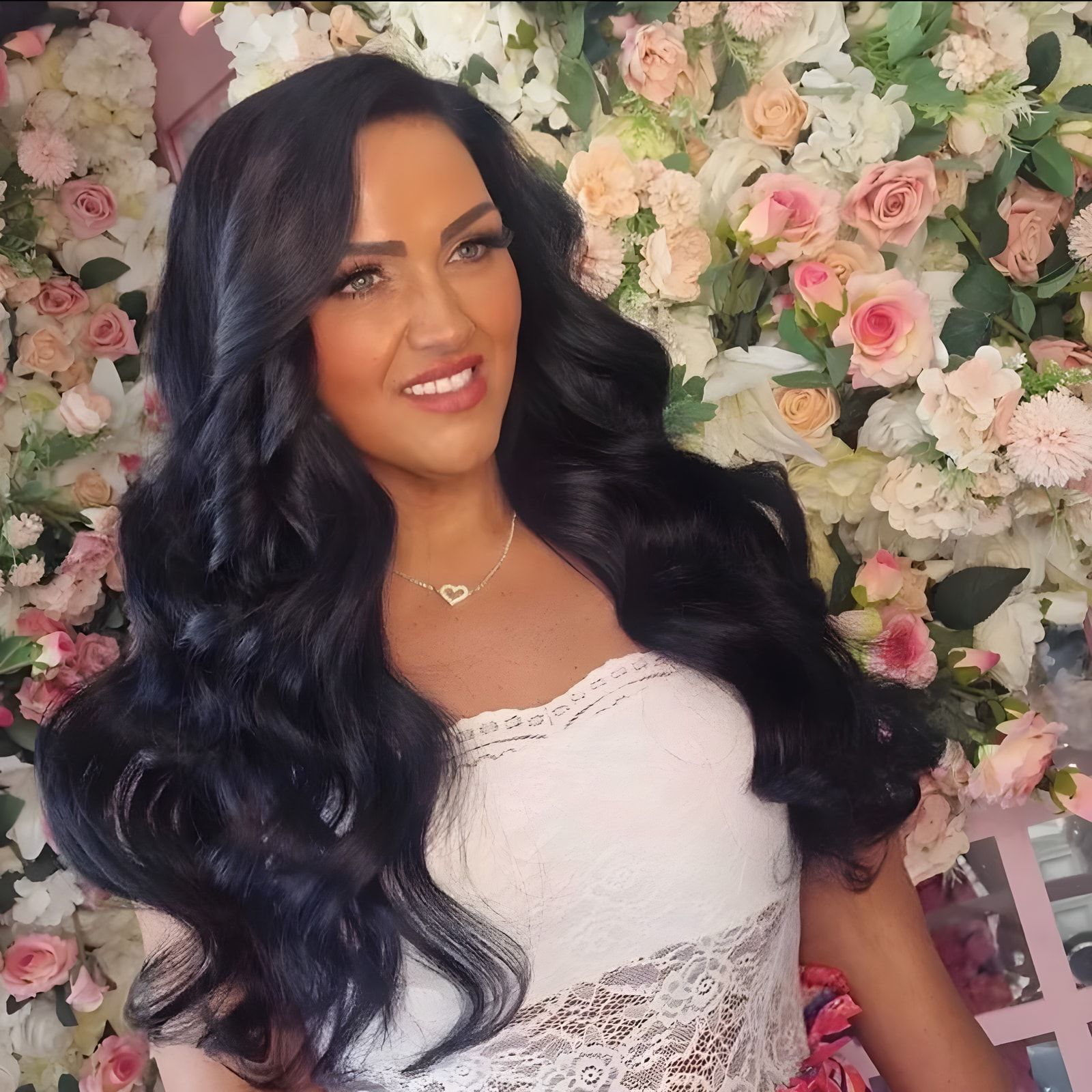 Lisa James with long, glossy dark waves in front of a pink and ivory flower wall